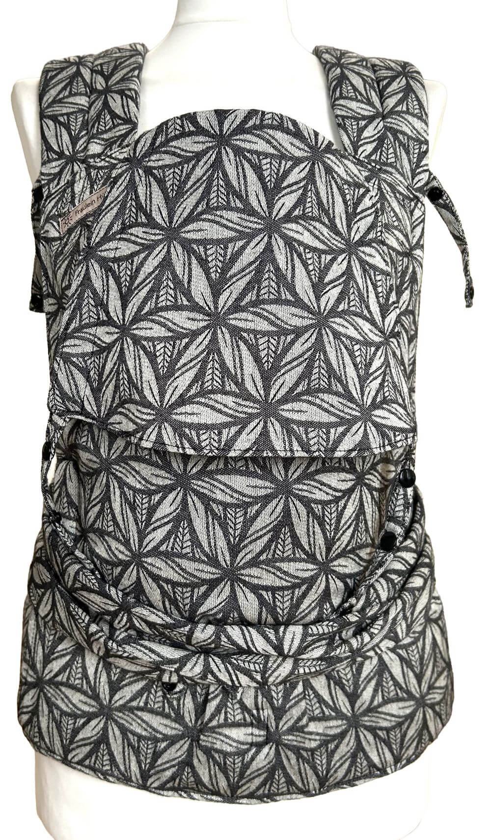 Babytrage mit Schulterträgern zum Binden und Hüftgurt mit Schnalle in grafischem Muster aus Weiß und Schwarz auf einer Schneiderbüste