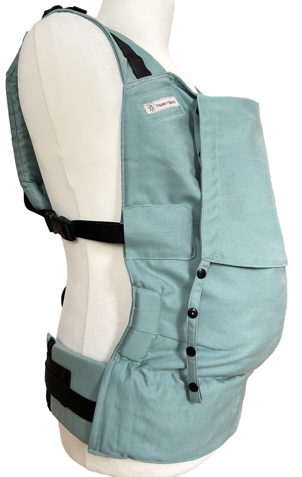 Fullbuckle Onesize Jade Seitlich Ruckenteil Fullbuckle Rucksacktrage in der Farbe Jadegrün auf einer Schneiderpuppe. Alle Gurt schließen mit SChnallen wie bei einem Rucksack, kein Binden. Man kann die Träger am Rückenteil und am Bauchgurt befestigen.