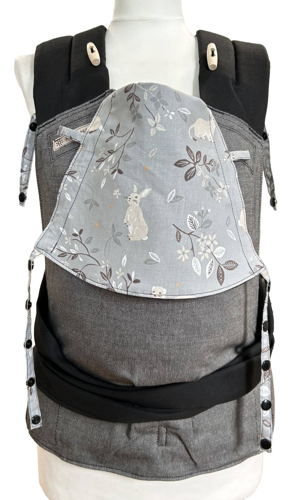 Fräulein Hübsch Babytrage Mei Tai in Dunkelgrau mit schwarzem Bauchgurt und Schulterträgern. Die Kopfstütze ist aus dunkelgrauem Dekostoff, auf dem ein Häschen, ein Wiesel, ein Dachs und ein Biber in Beige zu sehen sind. Dazwischen sind kleine Zweige abgebildet.