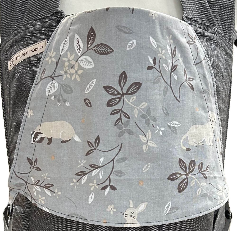 Detail des Kopfstützen-Stoffes: mittelgrauer Stoff mit dunkelgrauen und beigen Zweigen mit Blättern zwischen denen ein Dachs, ein Hermelin und ein Hase zu sehen sind.
