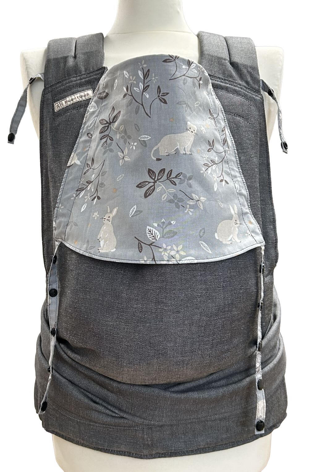 Babytrage von Fräulein Hübsch in Dunkelgrau mit mittelgrauer Kopfstütze mit kleinen Tieren wie Hermelin, Biber und Hase und Zweigen mit Blättern in Beige und Dunkelgrau. Die Babytrage schließt am Bauchgurt mit Schnalle und die SChulterträger sind zum Binden.