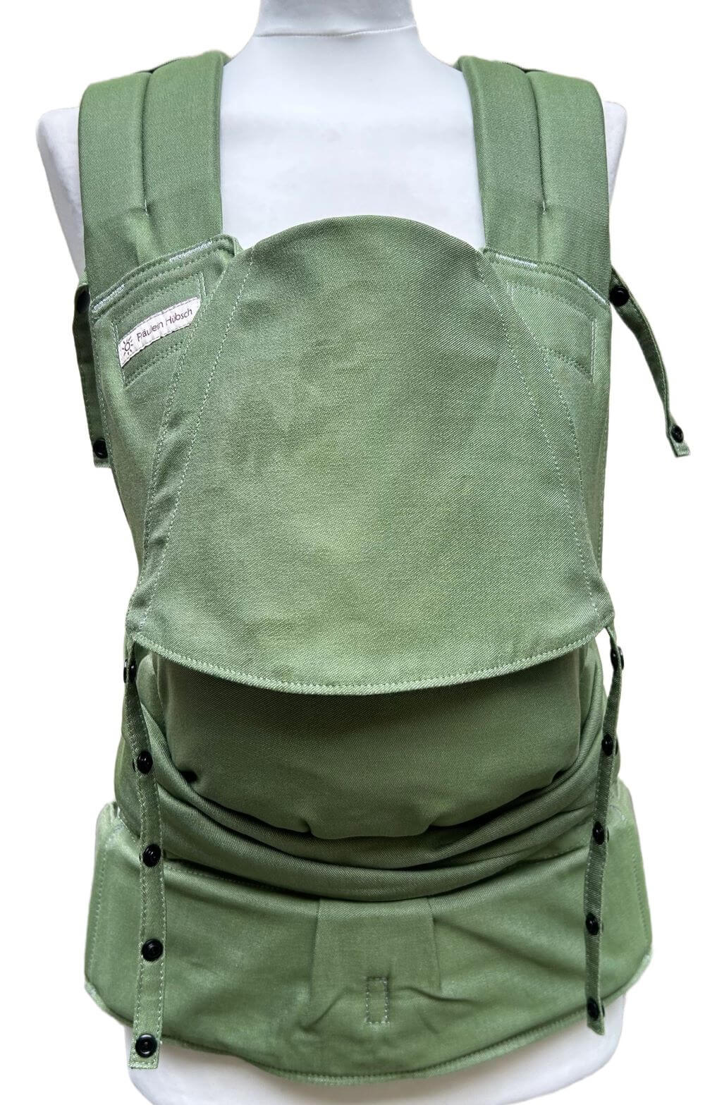 SoftTai V2 Babysize Kale Frontal_komp Babytrage von Fräulein Hübsch in hellem Olivgrün auf einer SChneiderpuppe. Der Hüftgurt schließt mit Schnalle, die Schulterträger sind zu binden.