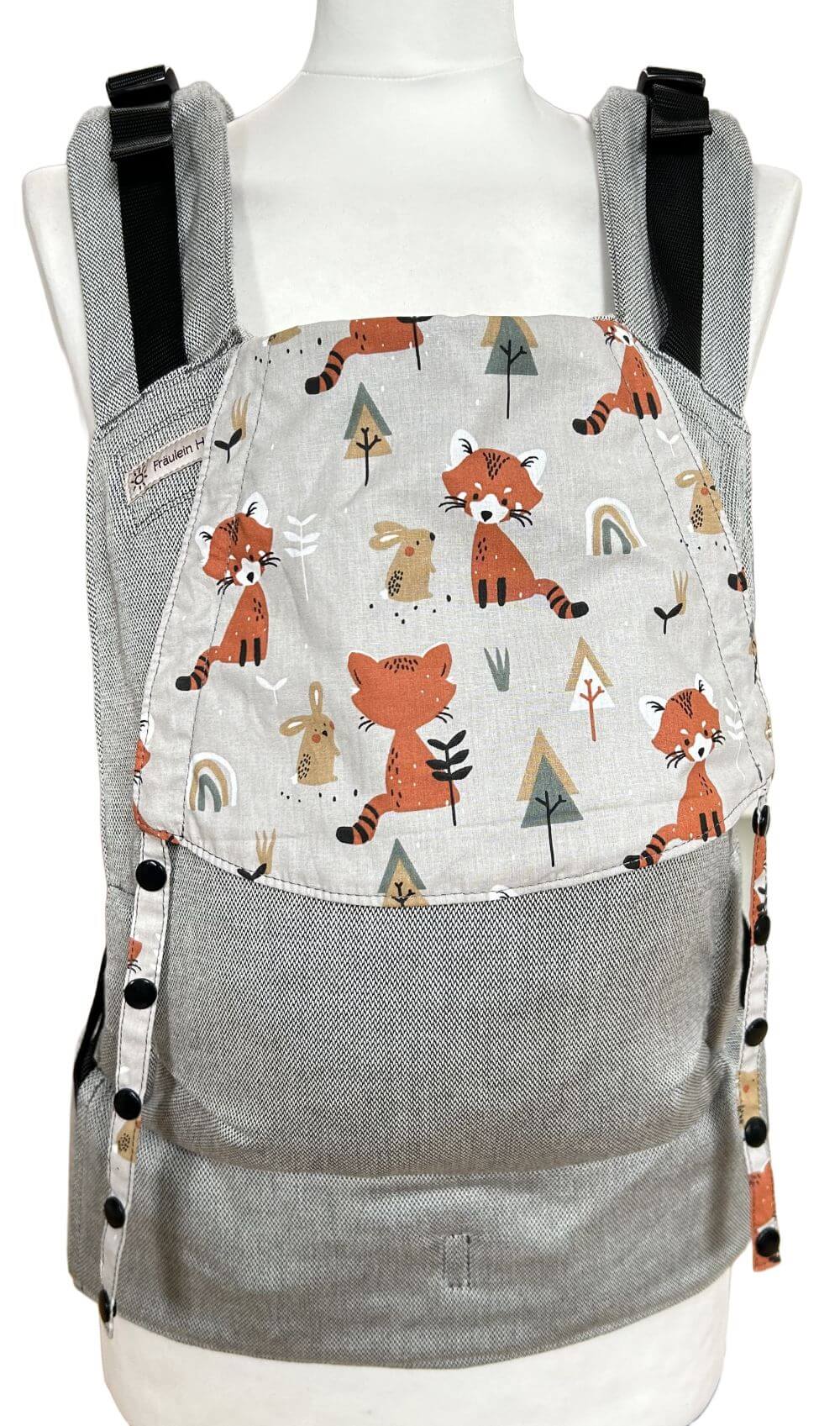 Fullbuckle Newborn Foxes frontal Fullbuckle Rucksacktrage Größe Newborn in Hellgrau mit einer Kopfstütze mit Füchsen auf Grau auf einer Schneiderbüste. Alle Gurte schließen mit Schnallen wie bei einem Rucksack, kein Binden.