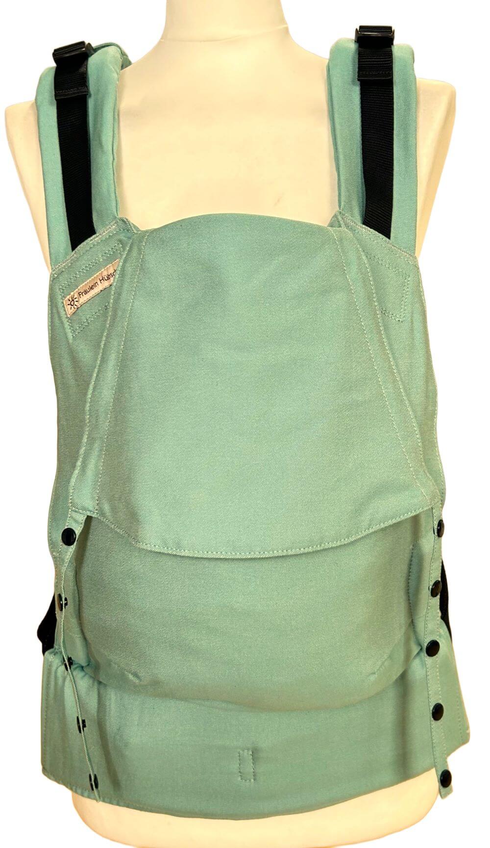 Fullbuckle Newborn Jade frontal Fullbuckle Rucksacktrage Größe Newborn in der Farbe Jade auf einer Schneiderbüste. Alle Gurte schließen mit Schnallen wie bei einem Rucksack, kein Binden.