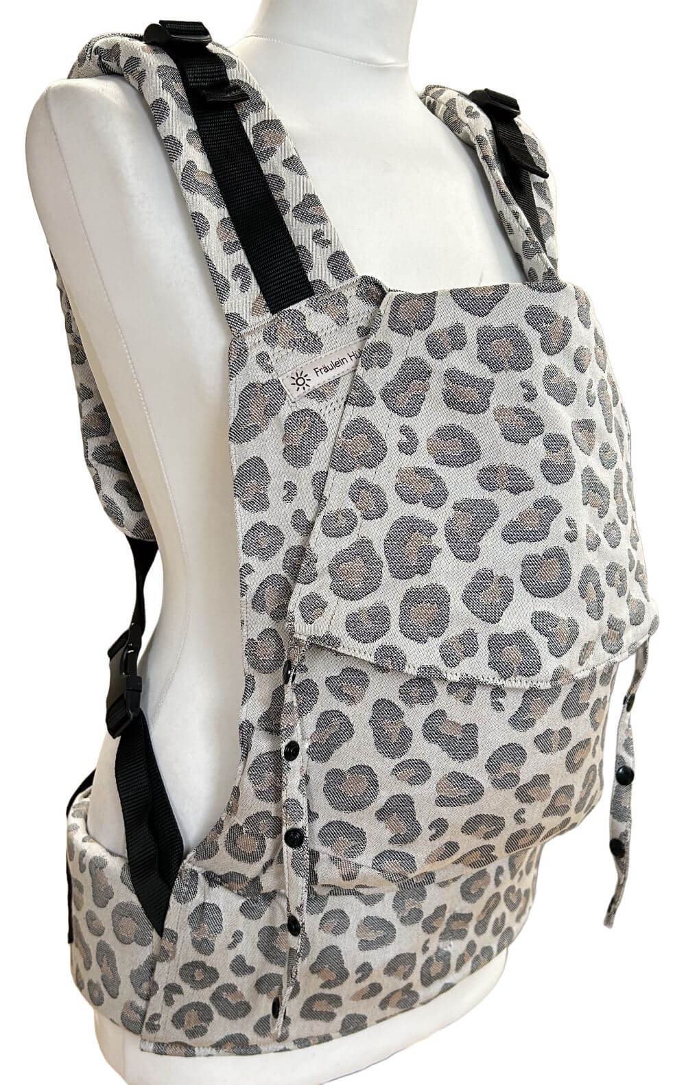 Fullbuckle Newborn Leoprint seitlich Fullbuckle Rucksacktrage Größe Newborn in der Farbe Leoprint auf einer Schneiderbüste. Alle Gurte schließen mit Schnallen wie bei einem Rucksack, kein Binden.