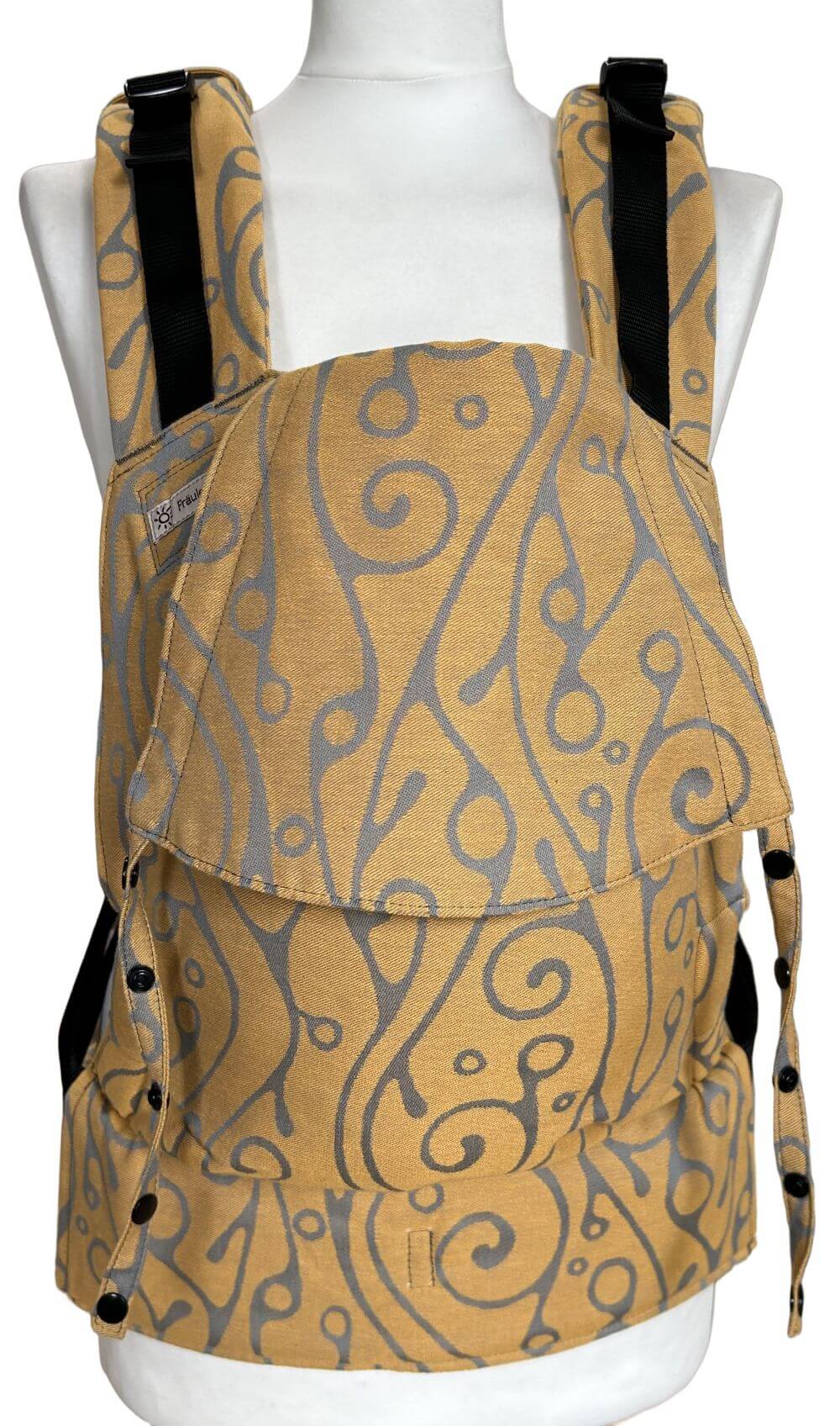 Fullbuckle Newborn Seaweed Bernstein frontal Fullbuckle Rucksacktrage Größe Newborn grauem Muster auf gelbem Grund auf einer Schneiderbüste. Alle Gurte schließen mit Schnallen wie bei einem Rucksack, kein Binden.