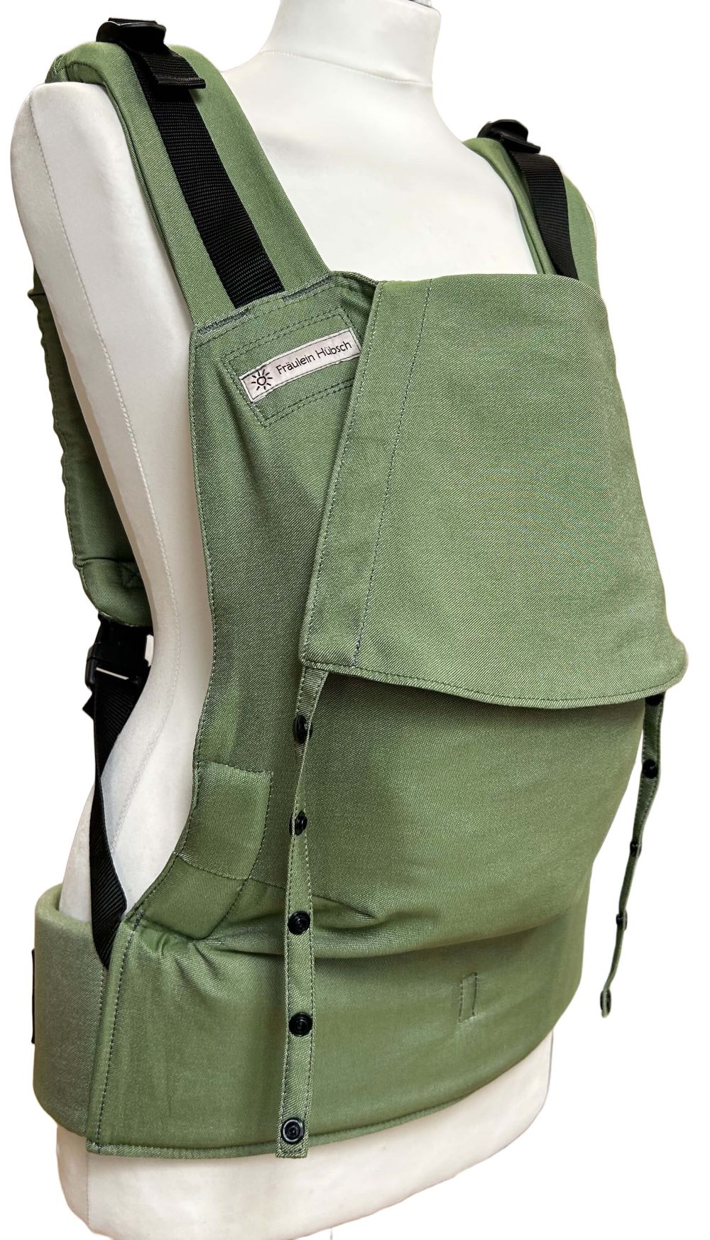 Fullbuckle Rucksacktrage Größe Newborn in der Farbe Kale auf einer Schneiderbüste. In der Trage sitzt eine Puppe. Alle Gurt schließen mit Schnallen wie bei einem Rucksack, kein Binden