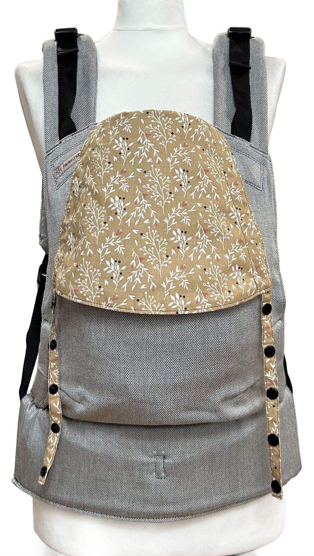 Fullbuckle Rucksacktrage Größe Newborn in Hellgrau mit einer Kopfstütze mit weißen Zweiglein auf Senfgelb auf einer Schneiderbüste. Alle Gurte schließen mit Schnallen wie bei einem Rucksack, kein Binden.