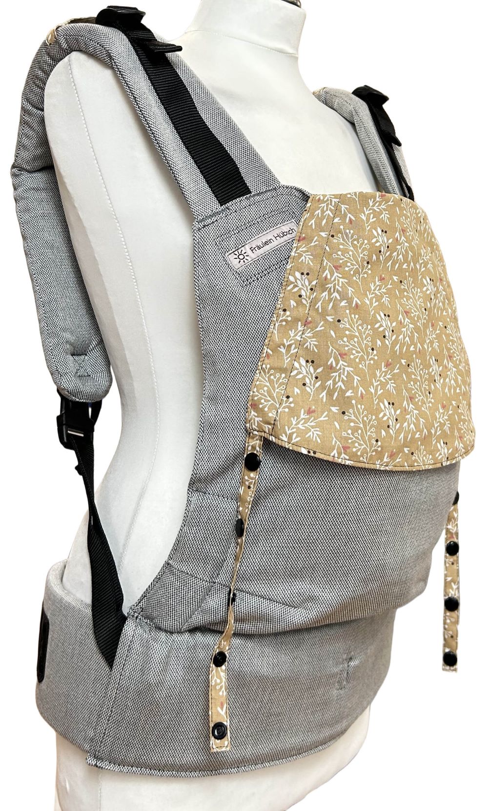 Fullbuckle Rucksacktrage Größe Newborn in Hellgrau mit einer Kopfstütze mit weißen Zweiglein auf Senfgelb auf einer Schneiderbüste. Alle Gurte schließen mit Schnallen wie bei einem Rucksack, kein Binden.