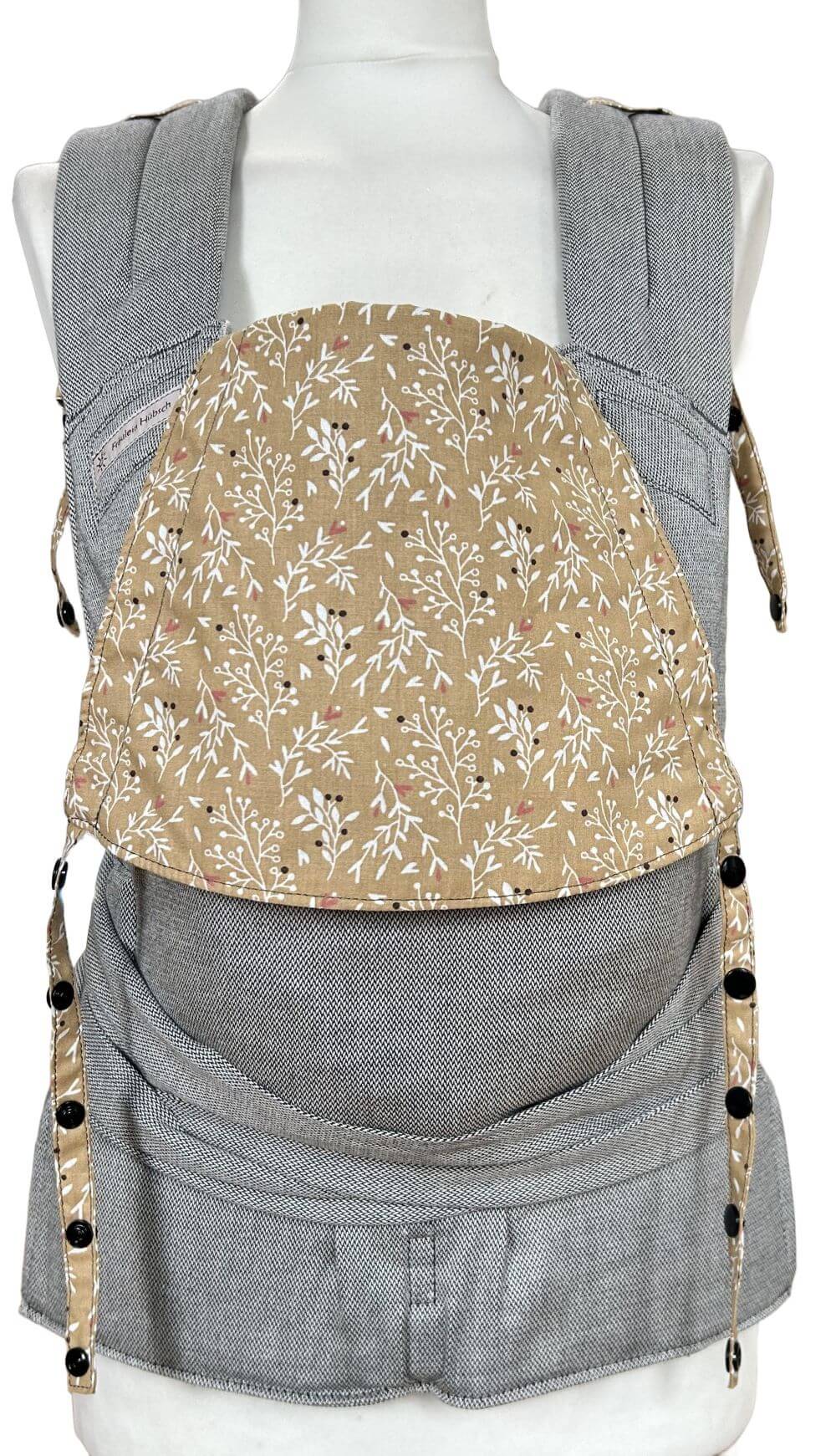 SoftTai V2 Babysize Silver Twigs Frontal Babytrage von Fräulein Hübsch in Hellgrau mit einer Kopfstütze mit weißen zarten Zweigen auf senfgelb auf einer SChneiderpuppe. Der Hüftgurt schließt mit Schnalle, die Schulterträger sind zu binden.