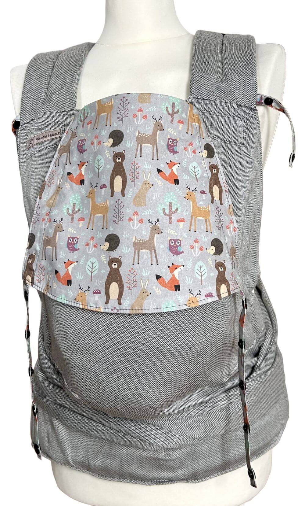 SoftTai V2 Toddlersize Magic Forest frontal Fräulein Hübsch SoftTai Toddlersize in Hellgrau mit bunter Kopfstütze, auf der bunte Waldtiere auf hellgrauem Grund abgebildet sind. Die Trage wird auf einer Schneiderpuppe gezeigt.