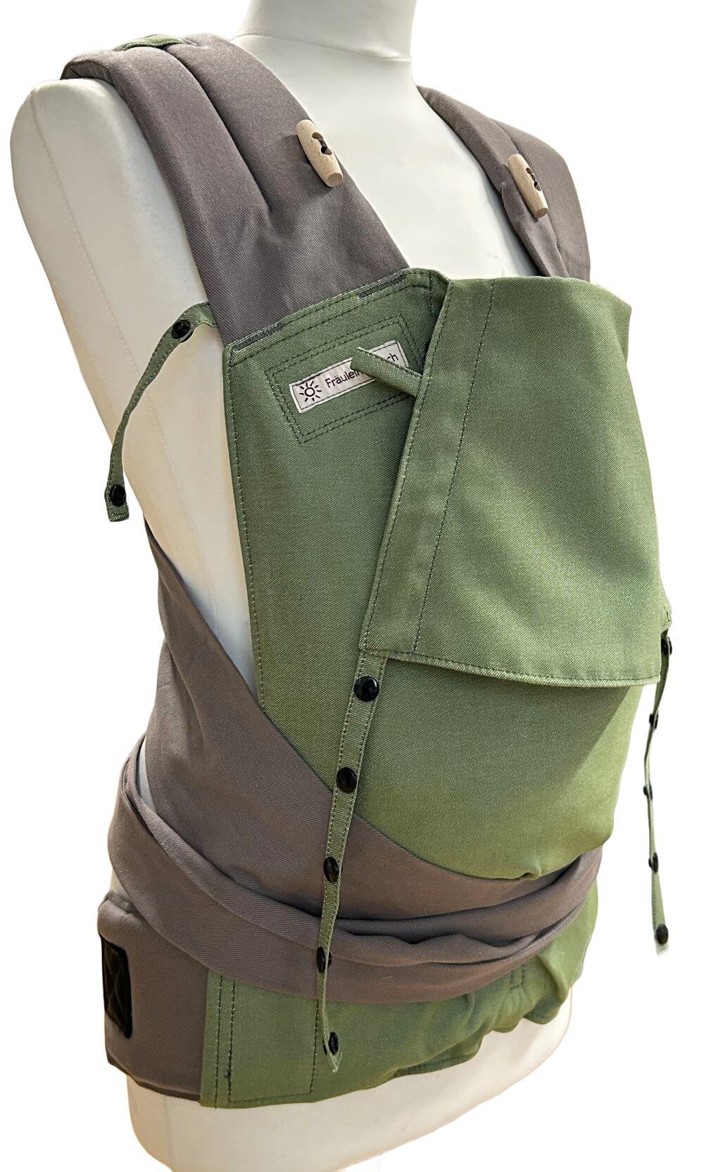 Mei Tai Babysize Kale seitlich Ergonomische Babytrage Fräulein Hübsch Mei Tai mit grauen Trägern und olivgrünem Rückenteil auf Schneiderbüste vor weißem Hintergrund.