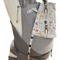 Fräulein Hübsch Babytrage Mei Tai Babysize in Hellgrau mit bunter Kopfstütze im Waldtier-Design auf hellgrauem Hintergrund, präsentiert auf einer Schneiderpuppe.