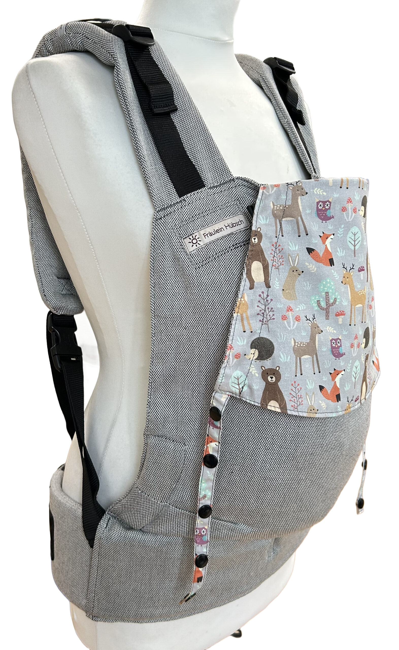 Fräulein Hübsch Fullbuckle Newborn in Hellgrau mit bunter Kopfstütze, auf der bunte Waldtiere auf hellgrauem Grund abgebildet sind. Die Trage wird auf einer Schneiderpuppe gezeigt.