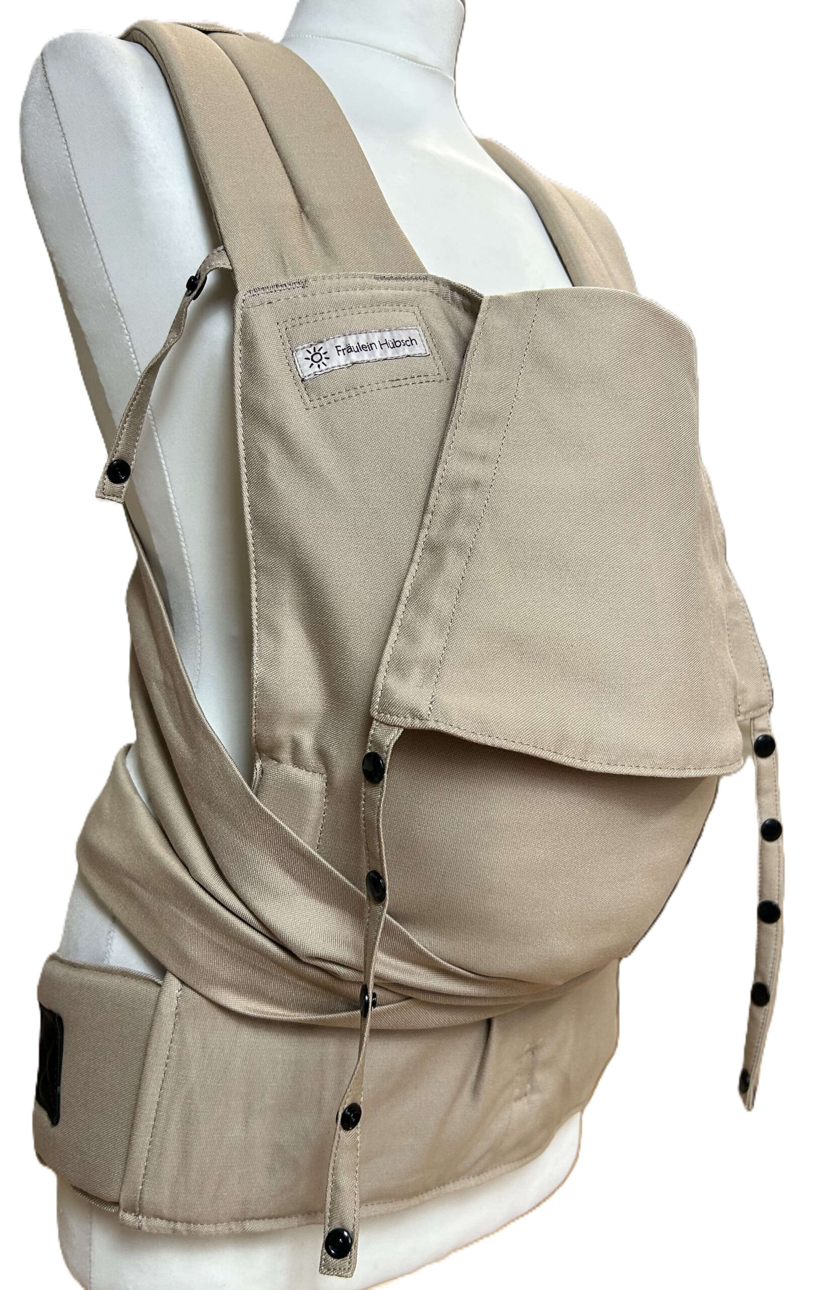 SoftTai Babytrage von Fräulein Hübsch in der Farbe Light Taupe auf einer Schneiderpuppe in frontaler Ansicht. Der Hüftgurt schließt mit Schnalle, die Schulterträger sind zu binden.