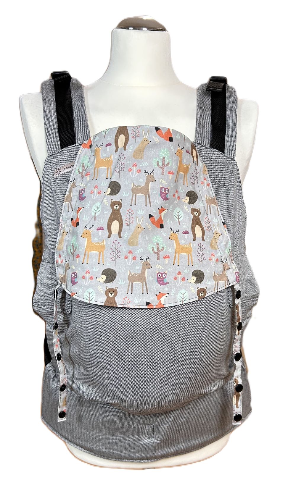 Fräulein Hübsch Fullbuckle Onesize in Hellgrau mit bunter Kopfstütze, auf der bunte Waldtiere auf hellgrauem Grund abgebildet sind. Die Trage wird auf einer Schneiderpuppe gezeigt.