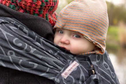 Baby in einer WrapCon von Fräulein Hübsch mit Mütze und Wollwalkoverall. Baby tragen im Winter.