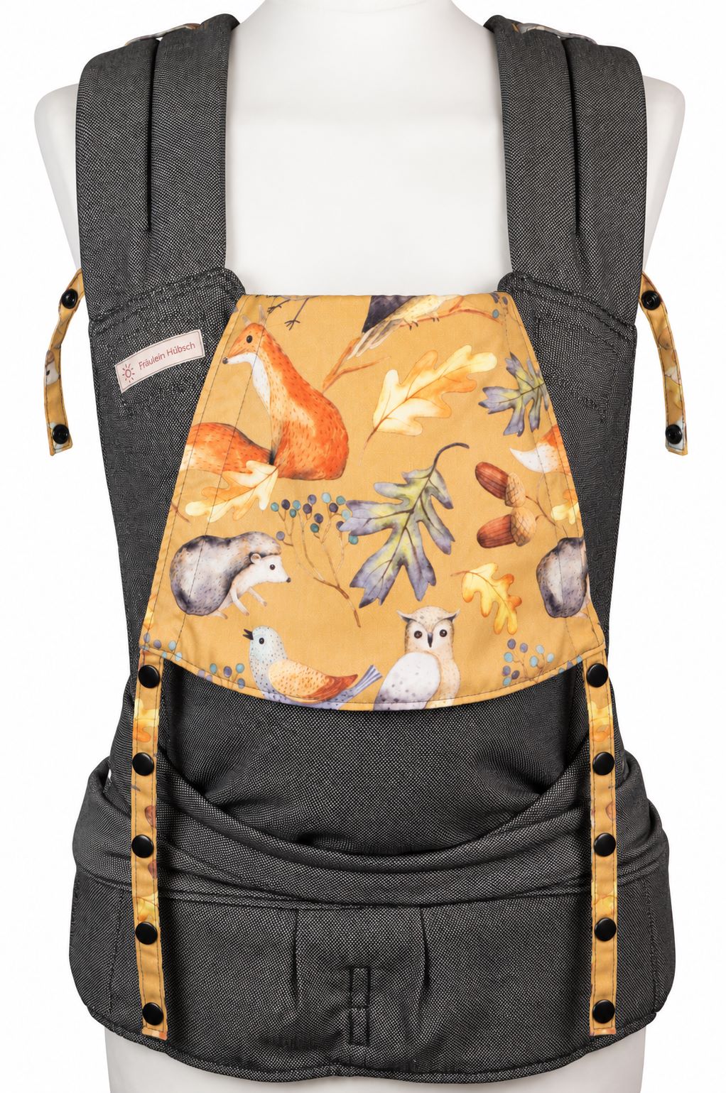 Fräulein Hübsch SoftTai Babysize in Dunkelgrau mit bunter Kopfstütze, auf der bunte Waldtiere wie Fuchs, Igel und Eule auf senfgelbem Grund abgebildet sind. Die Trage wird auf einer Schneiderpuppe gezeigt.